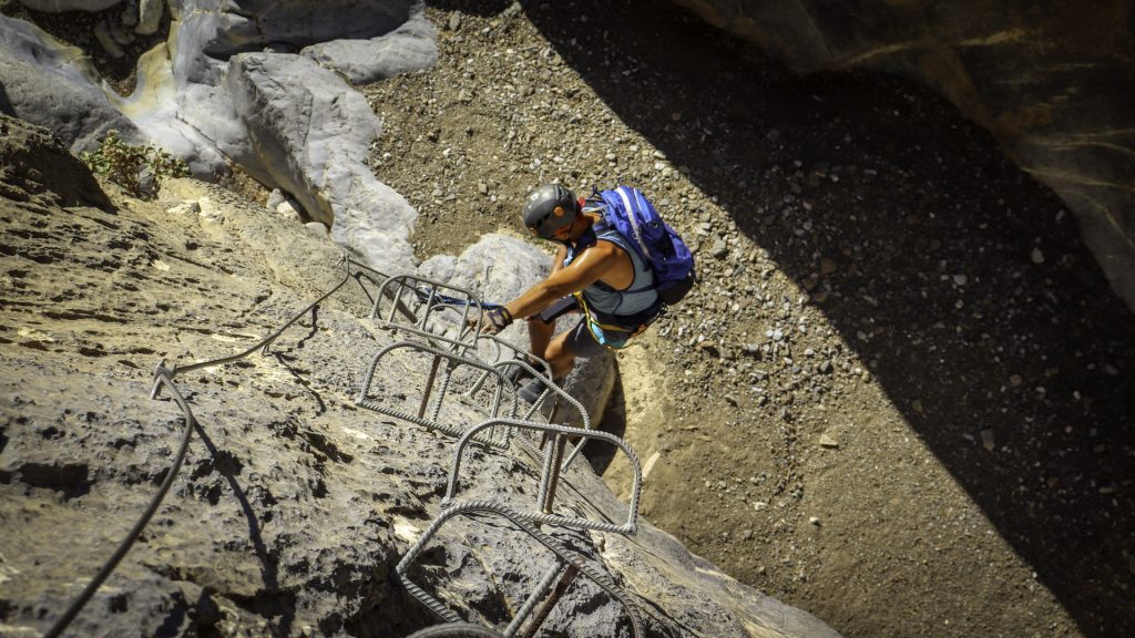 Hiker climbing a metal via ferrata ladder in the Asterousia Mountains.